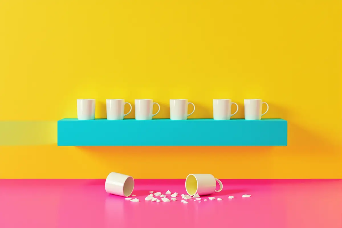 A shelf with an even row of identical white mugs, broken mugs and shards on the floor below